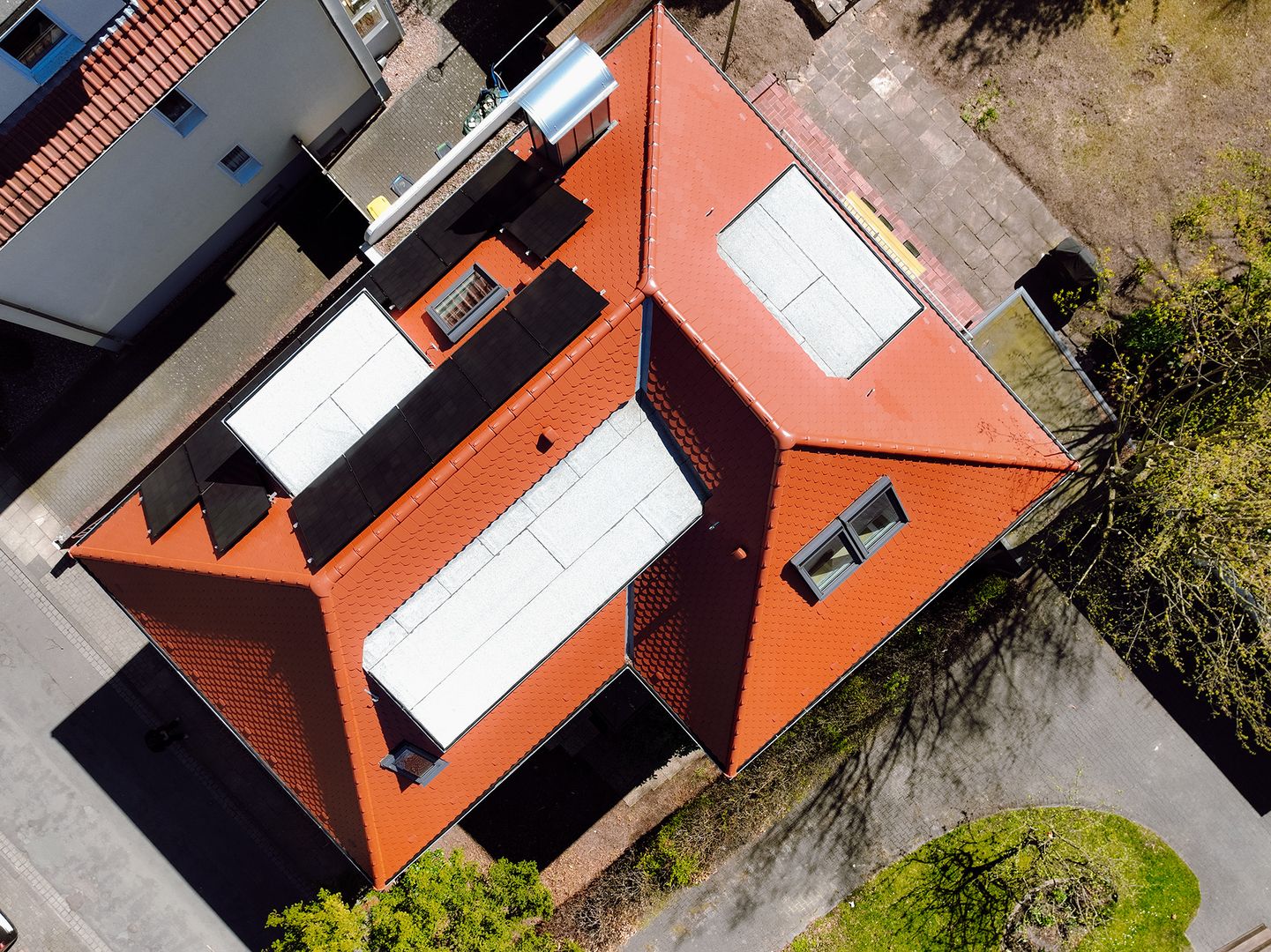Luftaufnahme eines sanierten Wohnhauses mit rotem Ziegeldach und moderner Photovoltaikanlage